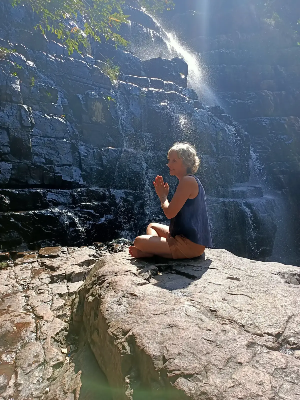 Christel en méditation, mains jointes, au pied d’une cascade